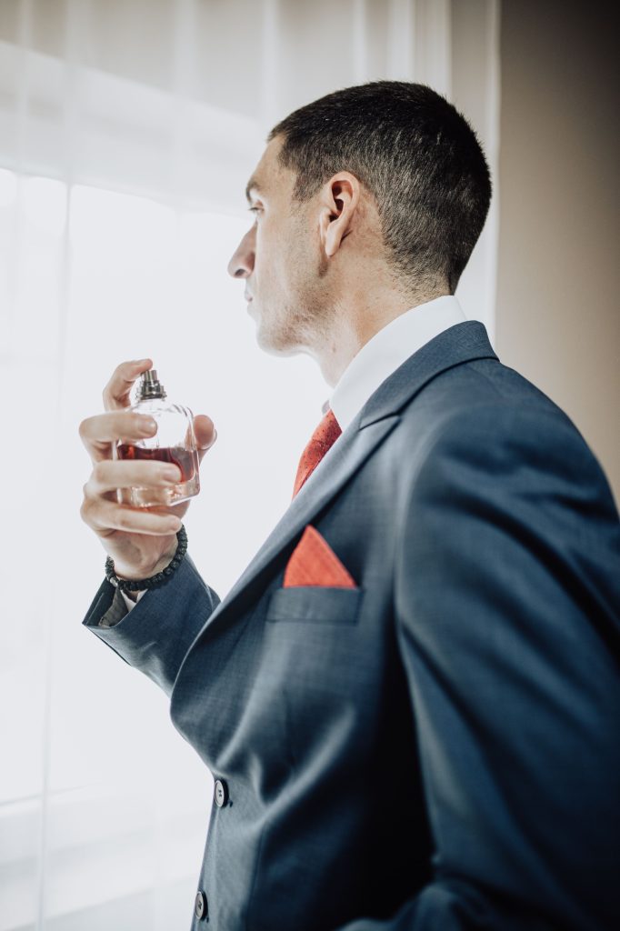 Vertical shot of a man in a suit looking through a window with a perfume in his hand